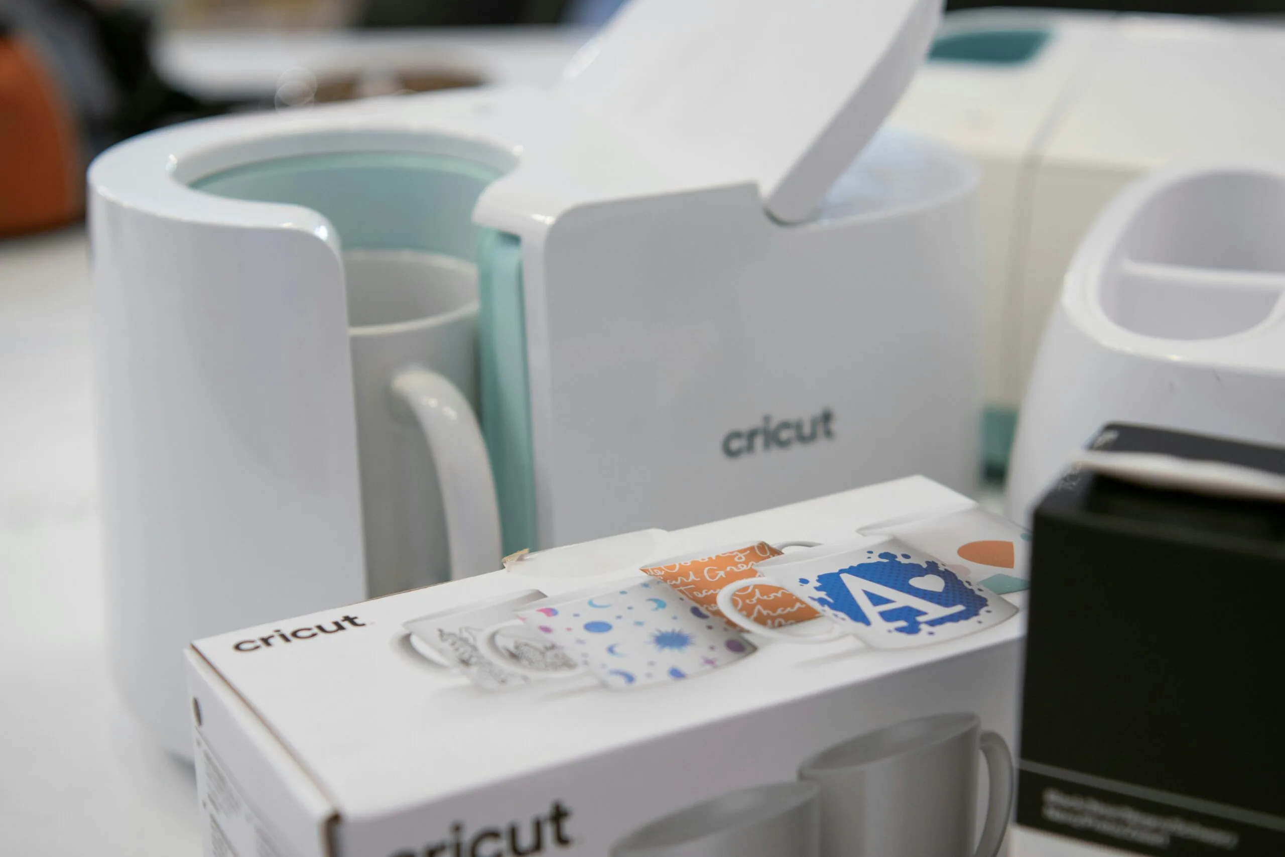 Mug Press and Cricut Heat Press Setup A Cricut mug press and accessories on a worktable, with a mug inside the press and a Cricut box in the foreground.