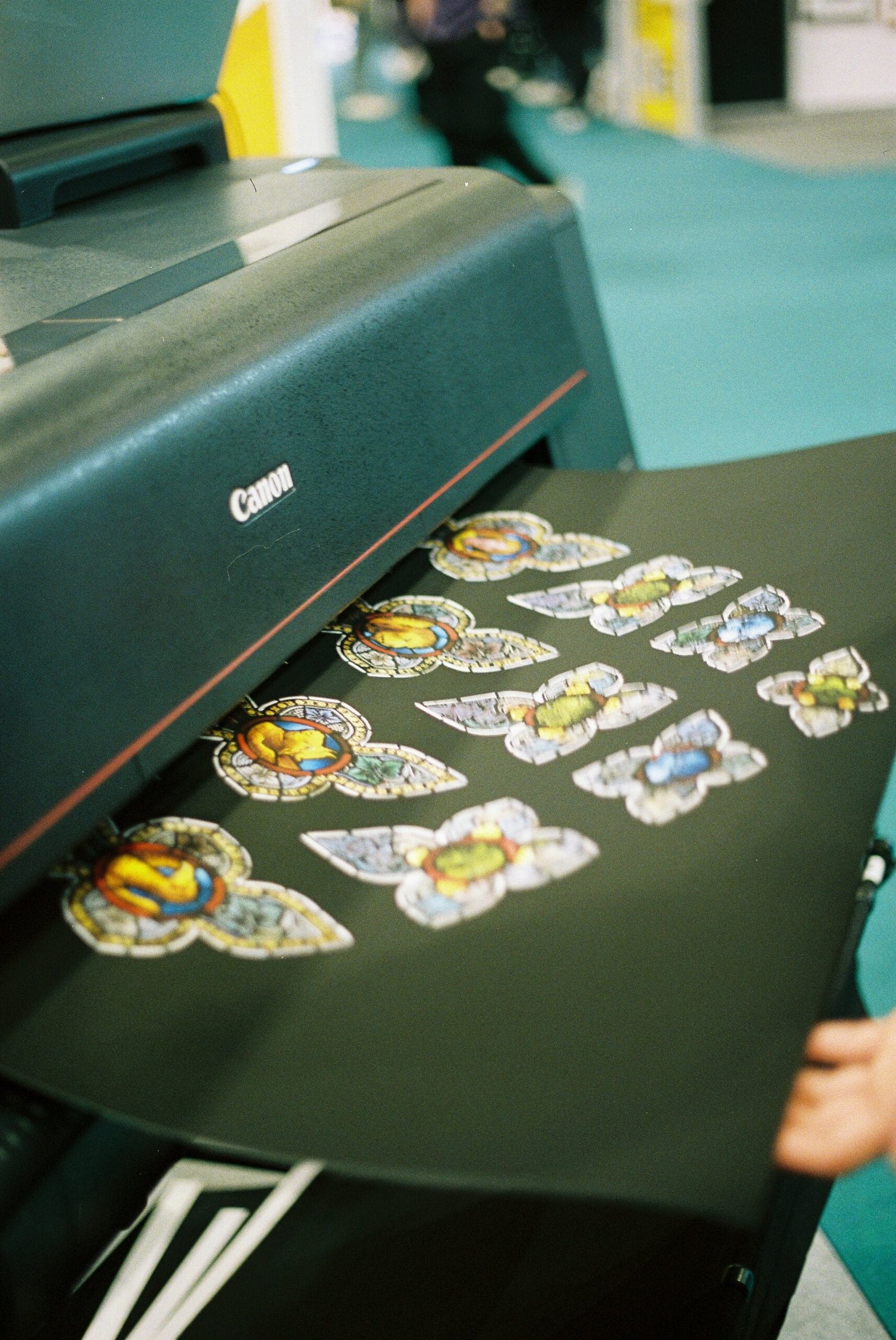 A close-up lifestyle photo showing someone handling a vinyl record beside a turntable on a wooden surface. The scene includes additional records and a small toy race car, giving it a relaxed, curated home music vibe. A Canon printer outputs a sheet of colorful custom stickers onto a black tray.